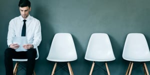 A young man in a shirt and tie seated in a row of white chairs, mastering behavioral interview questions from Green Flower on Careers in Cannabis 